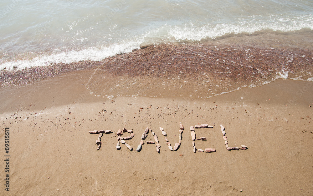 Fototapeta premium travel written on sandy beach near sea