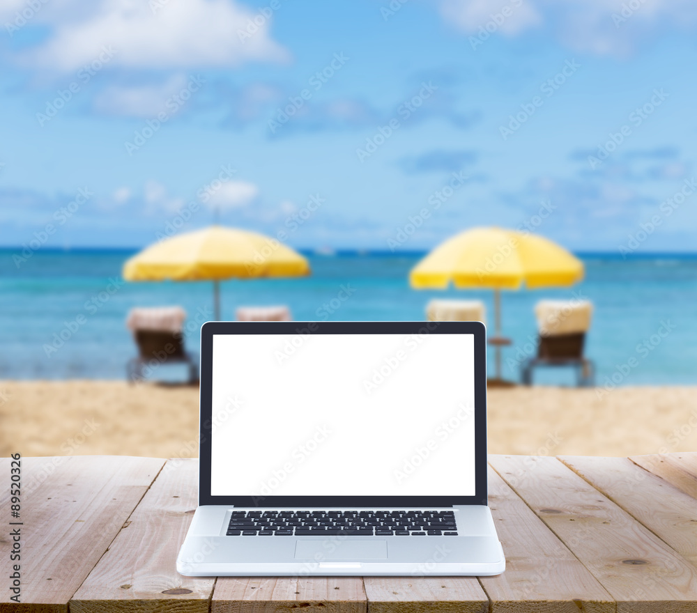 laptop computer on wood table with blur beach background