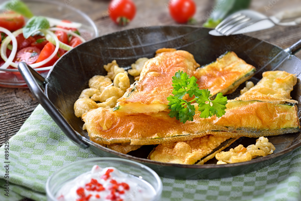 Krosse, panierte Zucchinischnitzel mit scharfer Dip-Soße und Tomatensalat serviert Krosse, panierte Zucchinischnitzel mit scharfer Dip-Soße und Tomatensalat serviert