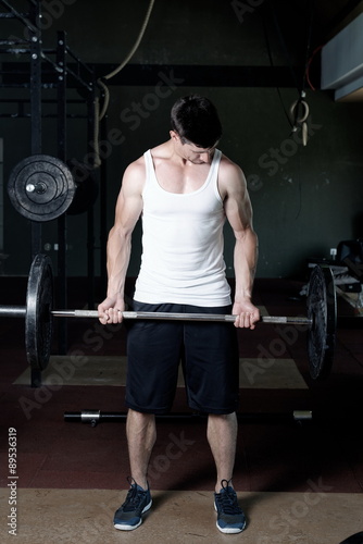 Close up of young muscular man lifting weights over dark background