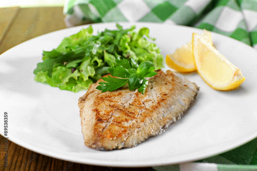 Dish of fish fillet with greens and lemon on plate close up Dish of fish fillet with greens and lemon on plate close up