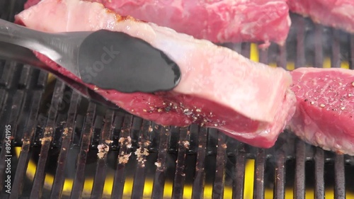 New York strip steaks being turned on a grill