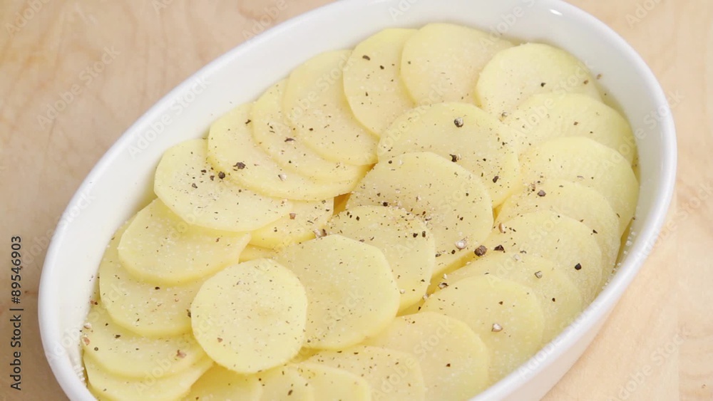Potato slices in a baking dish being seasoned with nutmeg Potato slices in a baking dish being seasoned with nutmeg