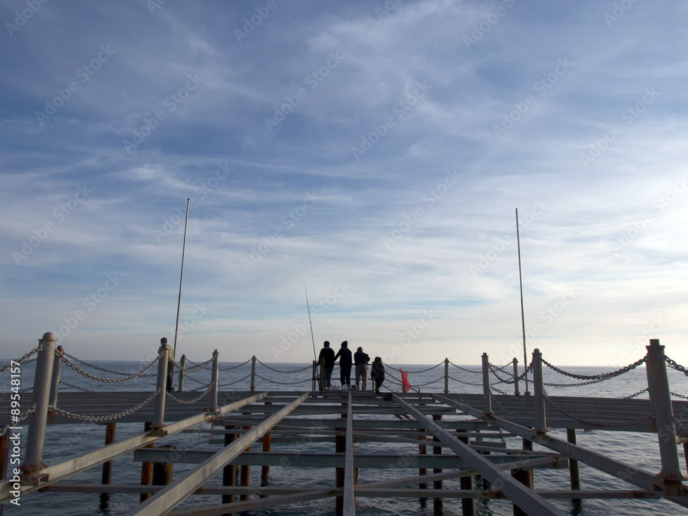 People silhouetted on a fishing pier at sunset People silhouetted on a fishing pier at sunset