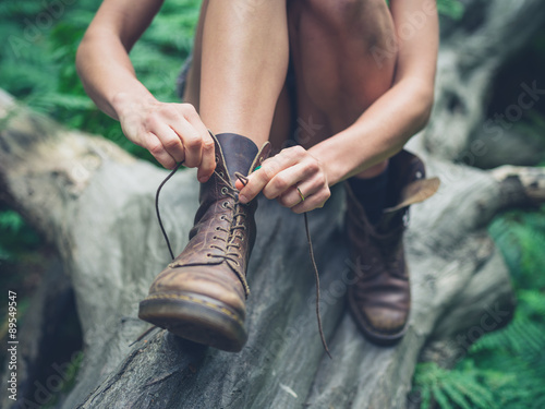Young woman tyoing her boots in forest photo