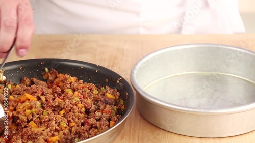 A minced meat and vegetable mixture being placed to a pie tin
