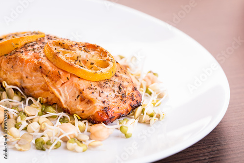 Portion of grilled salmon with lemon and sprouts.
