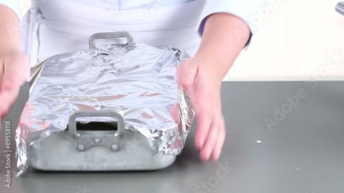 Moussaka in a baking dish being covered with aluminium foil
