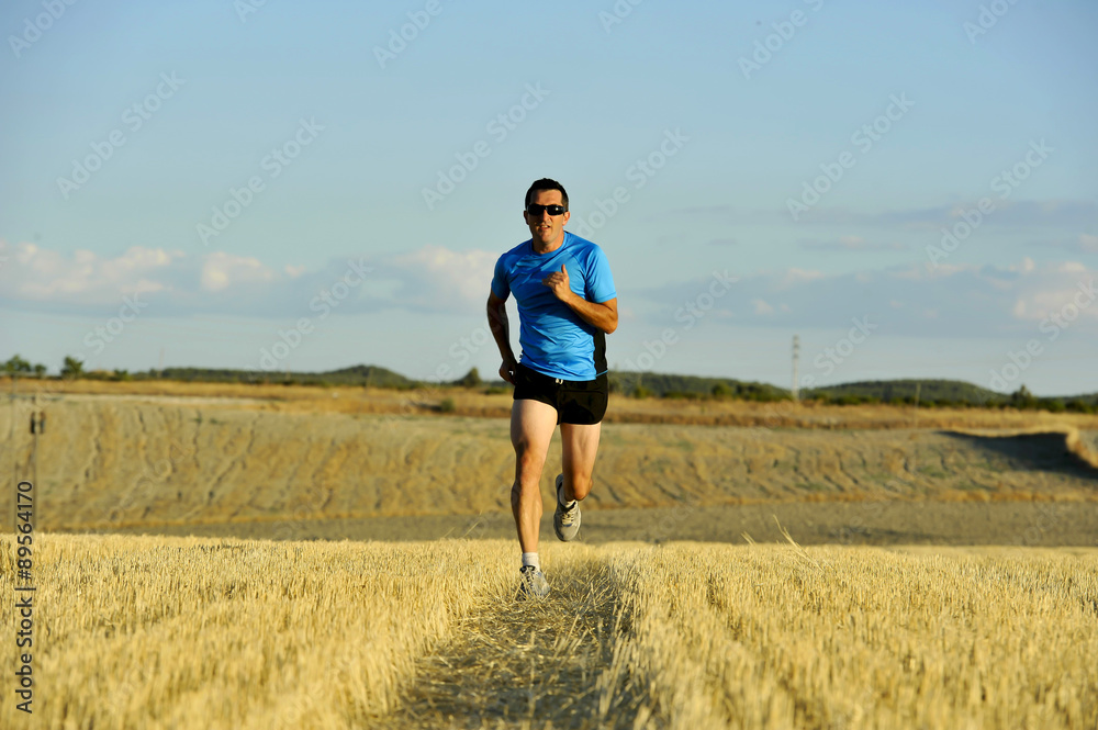 sport man with sunglasses running outdoors on straw field ground in frontal perspective