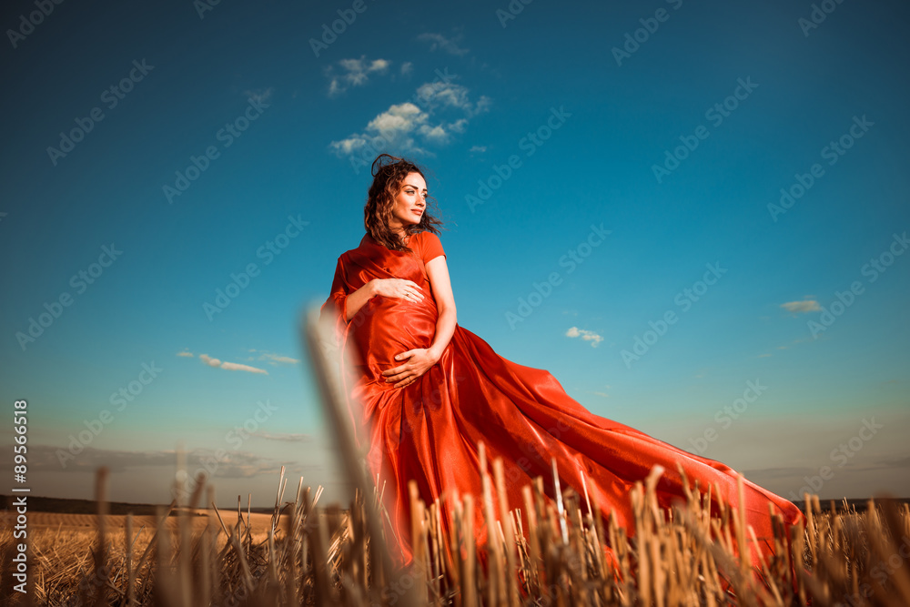 Obraz premium pregnant woman in red at windy sunset field