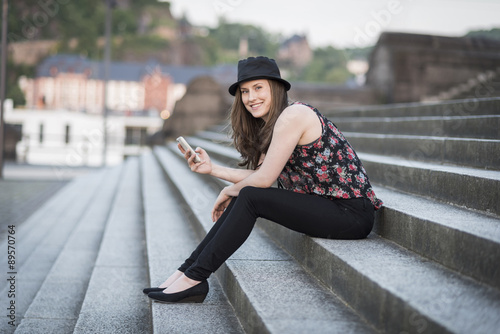 Germany, Koblenz, Deutsches Eck, young woman with cell phone sitting on stairs photo