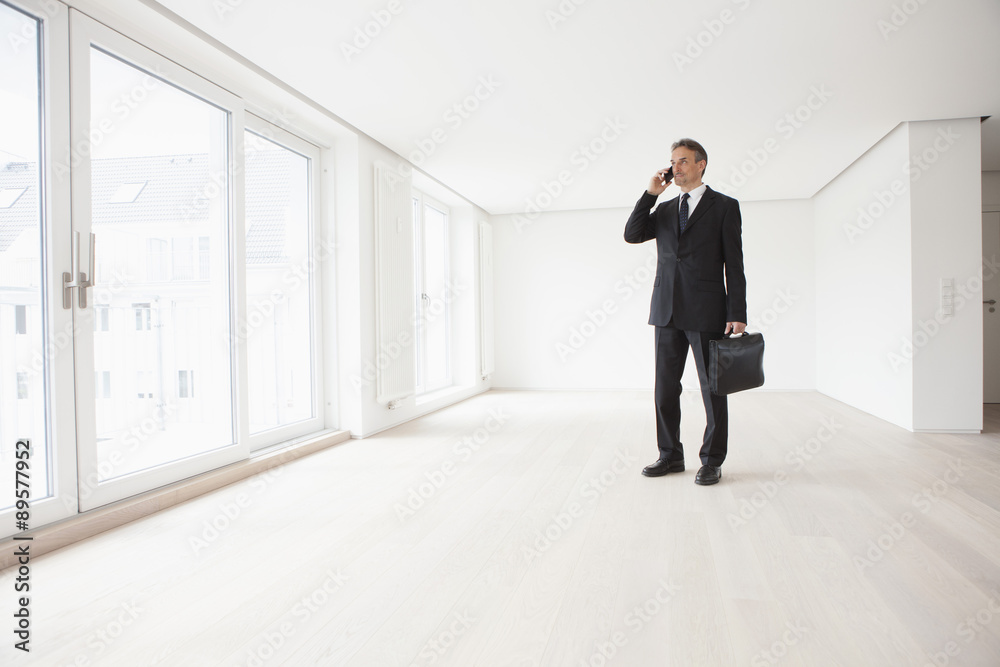 Estate agent standing in empty apartment, talking on the phone Estate agent standing in empty apartment, talking on the phone