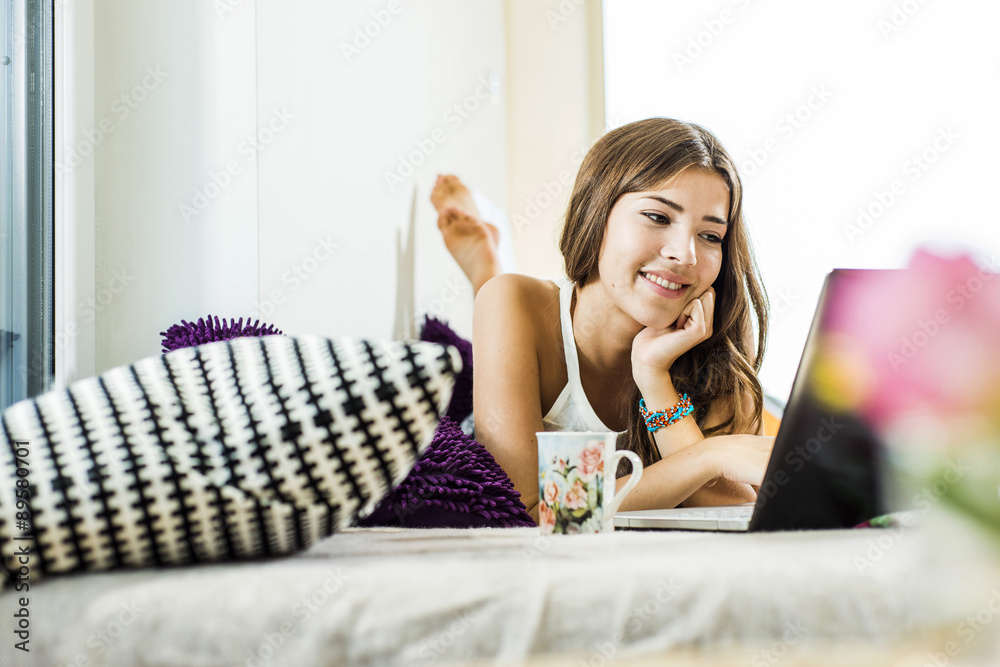 Relaxed young woman lying in bed using laptop Relaxed young woman lying in bed using laptop