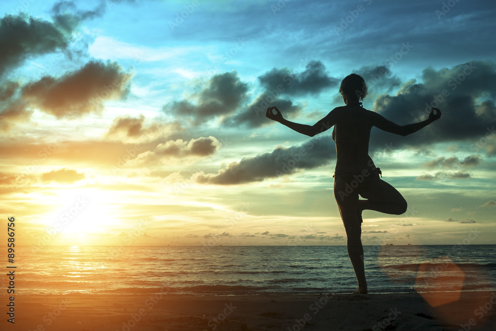 Silhouette of woman standing at yoga pose on the beach during an amazing sunset. Meditation, balance, harmony and tranquility concept.