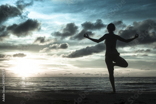 Silhouette of woman standing at yoga pose on the beach during an amazing sunset in cold gray-blue tones. Meditation, balance, harmony and tranquility concept.