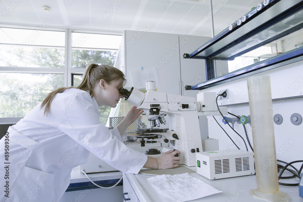 Young natural scientist using optical microscope in a laboratory Young natural scientist using optical microscope in a laboratory