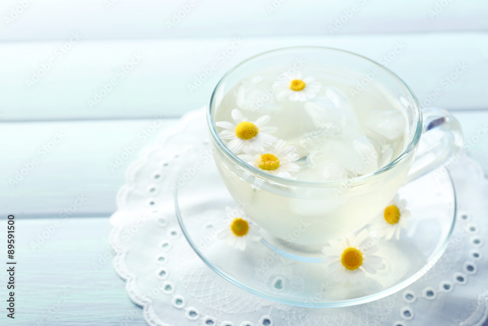 Glass of cold chamomile tea with ice cubes and chamomile flowers on color wooden background