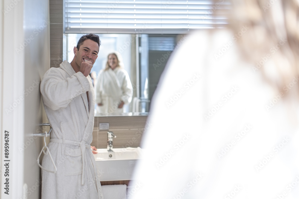 Man brushing his teeth in a hotel bathroom while his wife watching him Man brushing his teeth in a hotel bathroom while his wife watching him