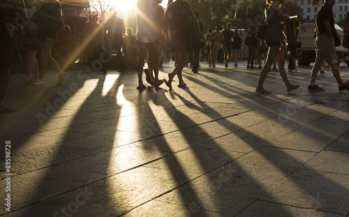 Crowds walking in a busy district as the sun flares between them in the late afternoon photo