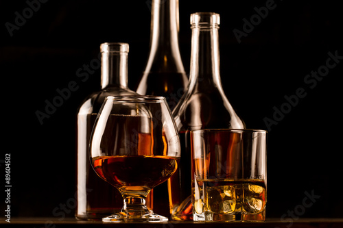 glass of whiskey with ice and a bottle on a wooden table. Cognac, brandy.