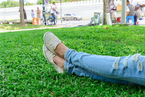 Cropped woman legs in denim with white sneakers resting on grass