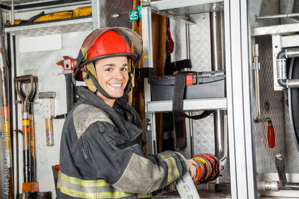 Fototapeta premium Happy Firefighter Fixing Water Hose In Truck