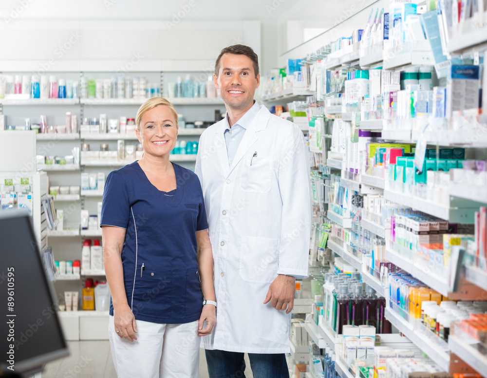 Confident Pharmacist And Assistant Standing In Pharmacy