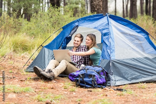 Young pretty hiker couple sitting in a tent looking at laptop