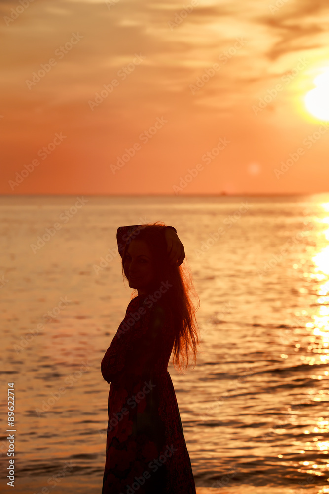 slim girl in long dress against sunrise over sea