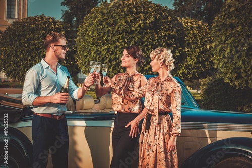 Sticker Wealthy friends drinking champagne near classic convertible