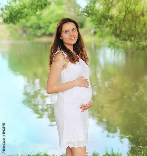 Portrait of beautiful young smiling pregnant woman in white dres