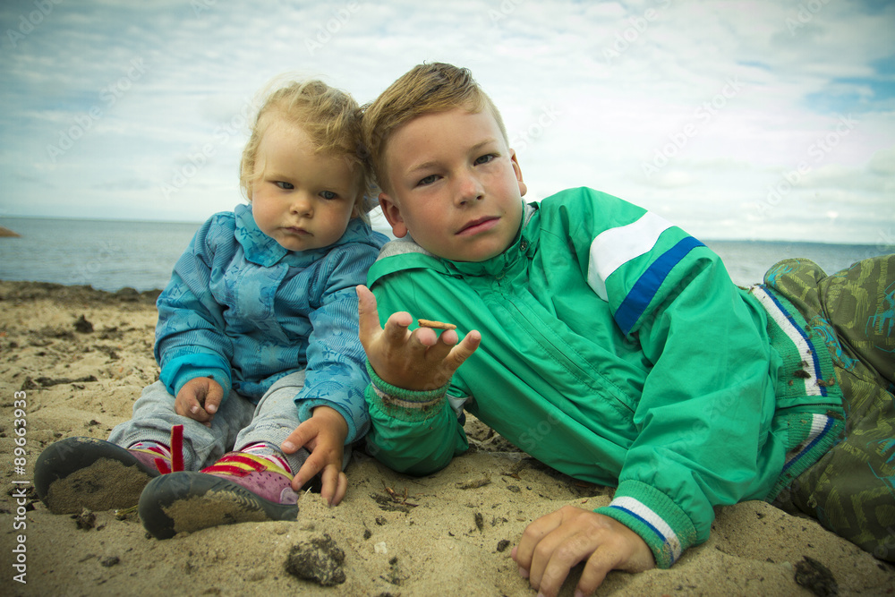 little girl sitting with her brother on the beach . little girl sitting with her brother on the beach .