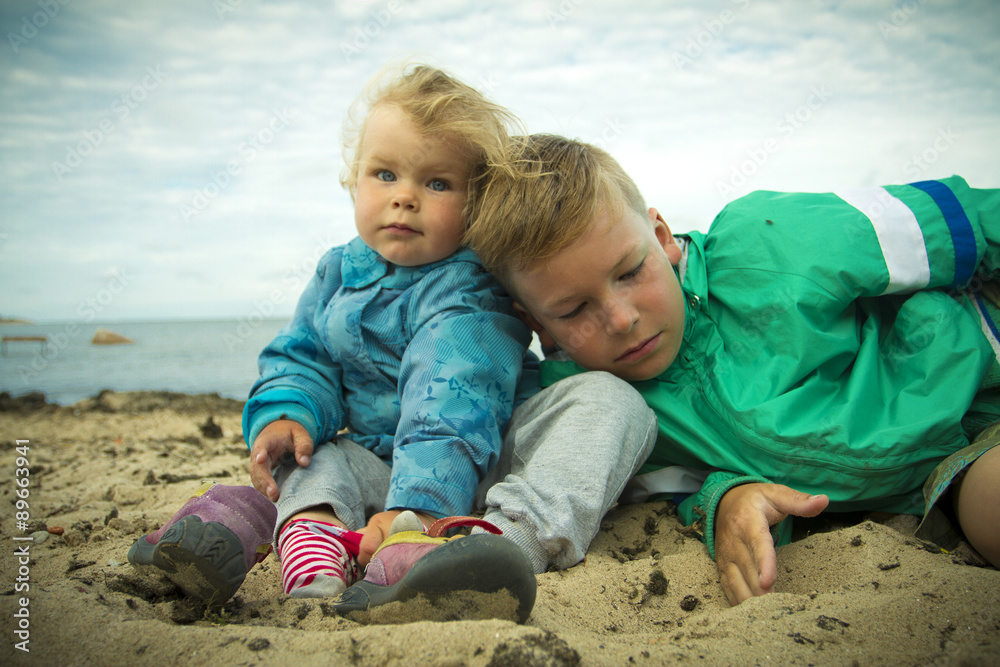 little girl sitting with her brother on the beach . little girl sitting with her brother on the beach .