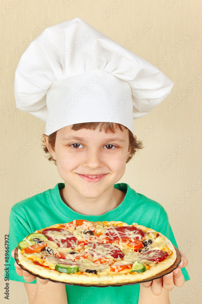 Young smiling boy in chefs hat with a cooked homemade pizza Young smiling boy in chefs hat with a cooked homemade pizza