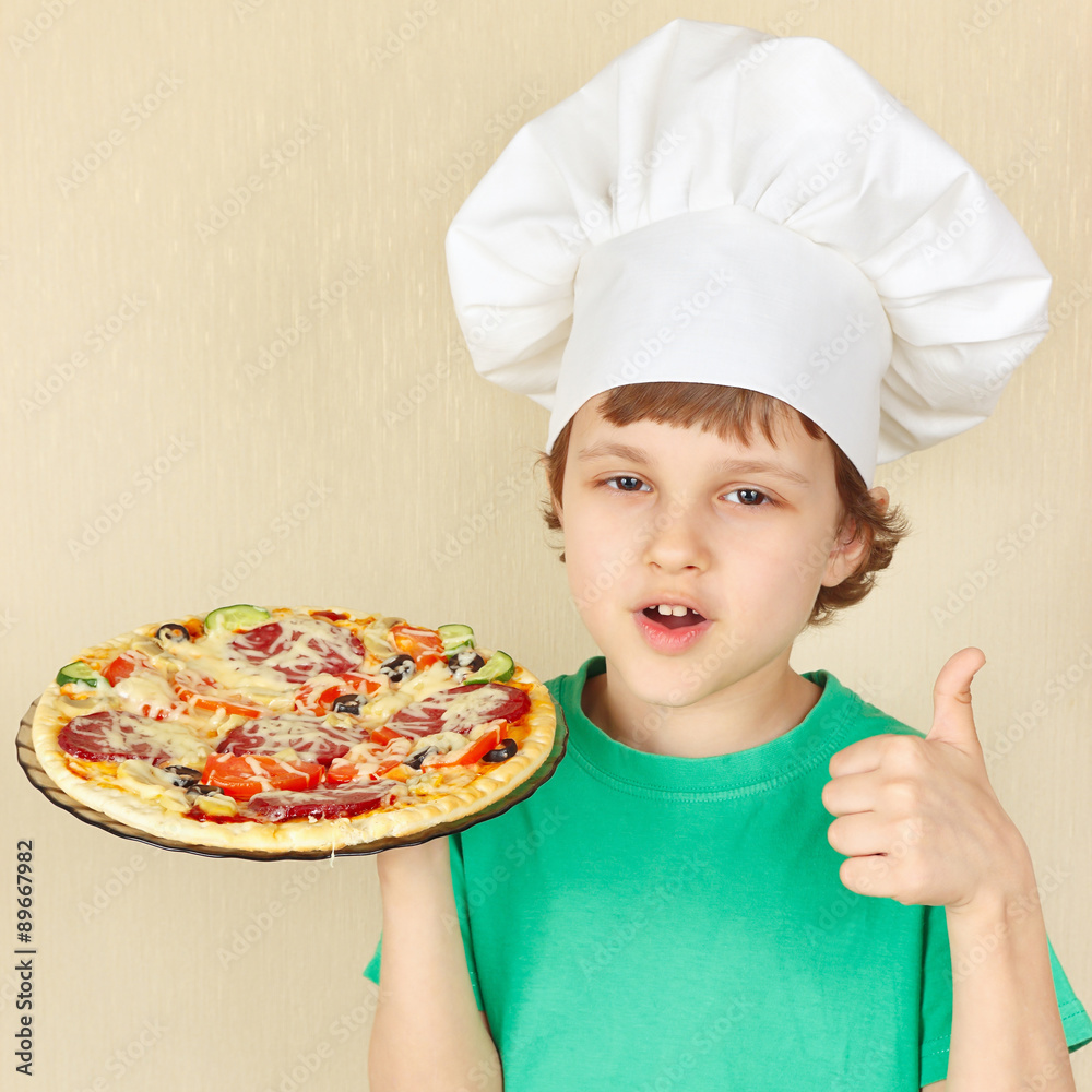 Little smiling kid in chefs hat with a cooked appetizing pizza Little smiling kid in chefs hat with a cooked appetizing pizza