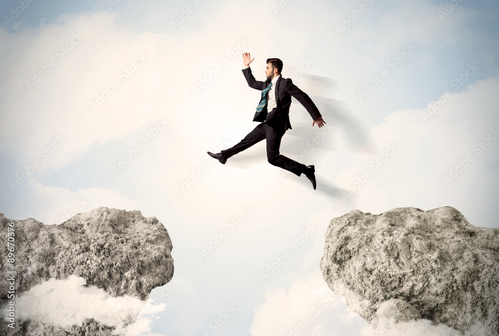Happy business man jumping over a cliff