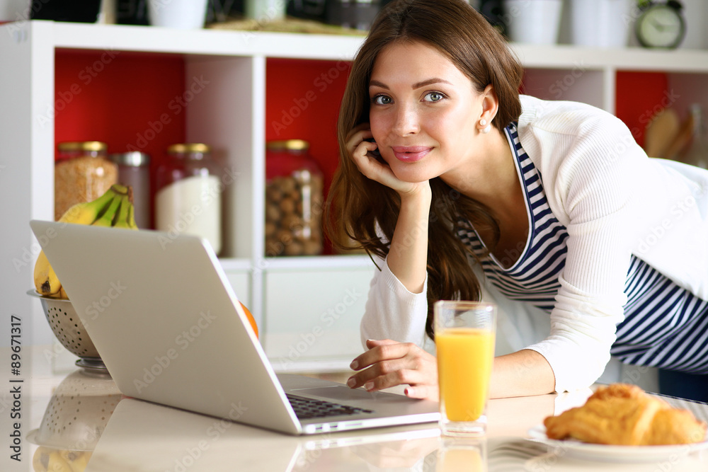 Attractive young woman using laptop and sitting in the kitchen Attractive young woman using laptop and sitting in the kitchen