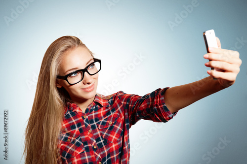 Close up portrait of a young joyful blonde girl holding a smartp photo