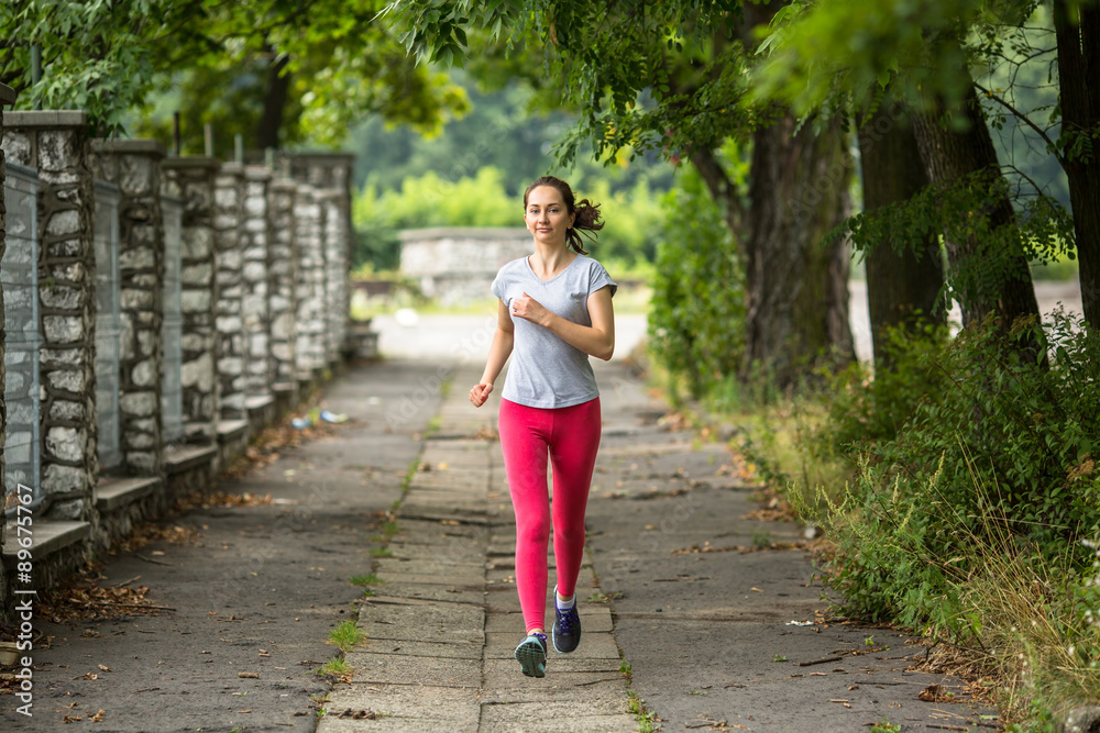 Young woman running on the track through the summer park. Training outdoors. Workout in a Park. Young woman running on the track through the summer park. Training outdoors. Workout in a Park.