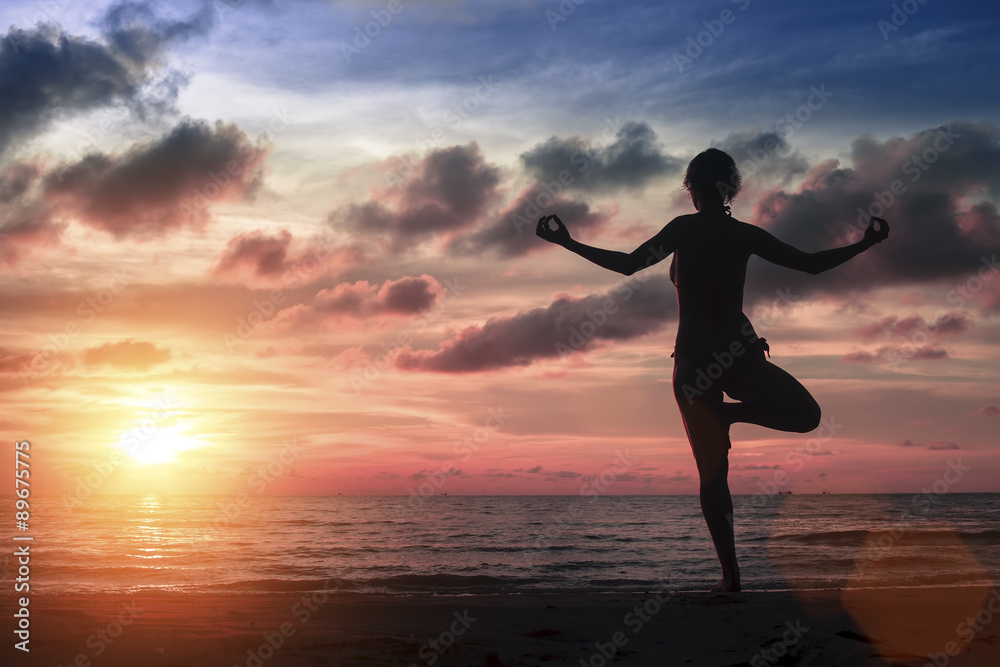 Silhouette young woman practicing yoga on the sea beach at amazing bloody sunset.