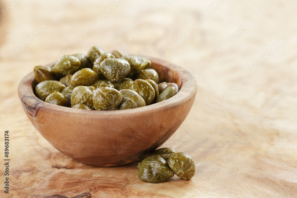 marinated capers in bowl on olive board marinated capers in bowl on olive board