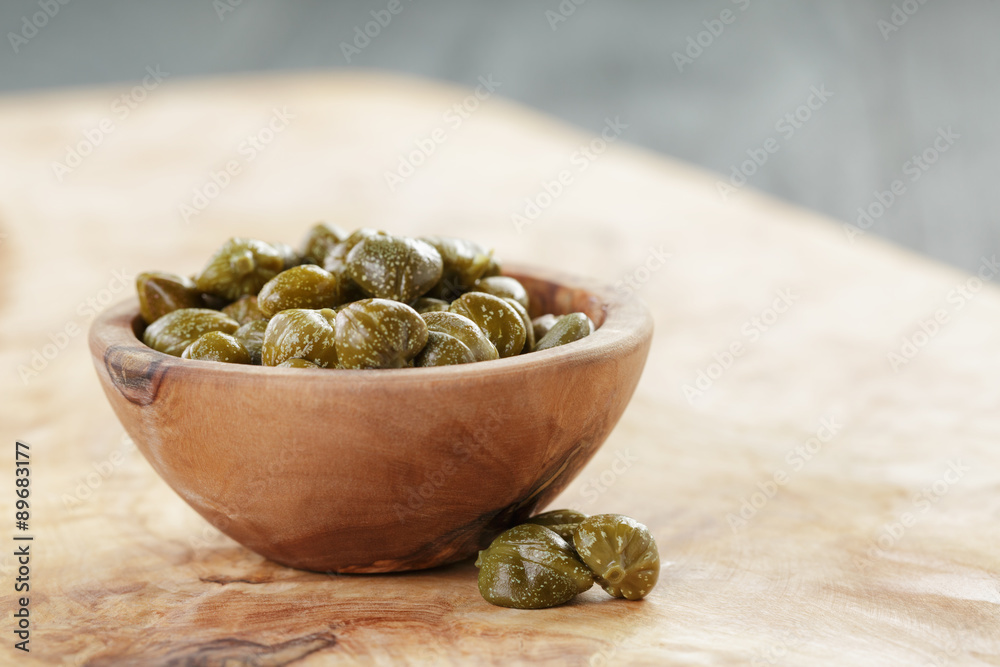 marinated capers in bowl on olive board marinated capers in bowl on olive board