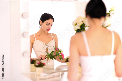 Beautiful young ballerina standing against mirror and looking at