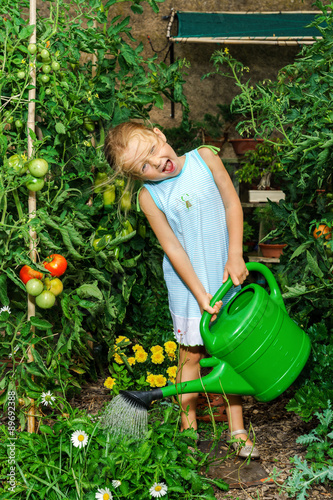Cute little girl watering tomato and flowers in the backyard