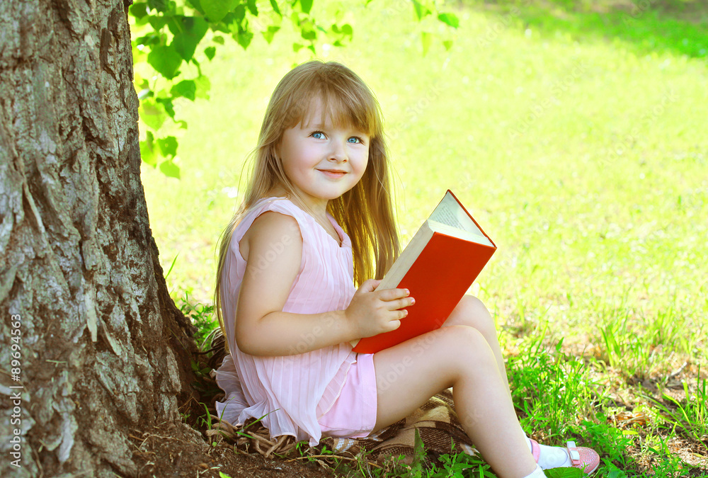 Little smiling girl child reading a book on the grass near tree Little smiling girl child reading a book on the grass near tree