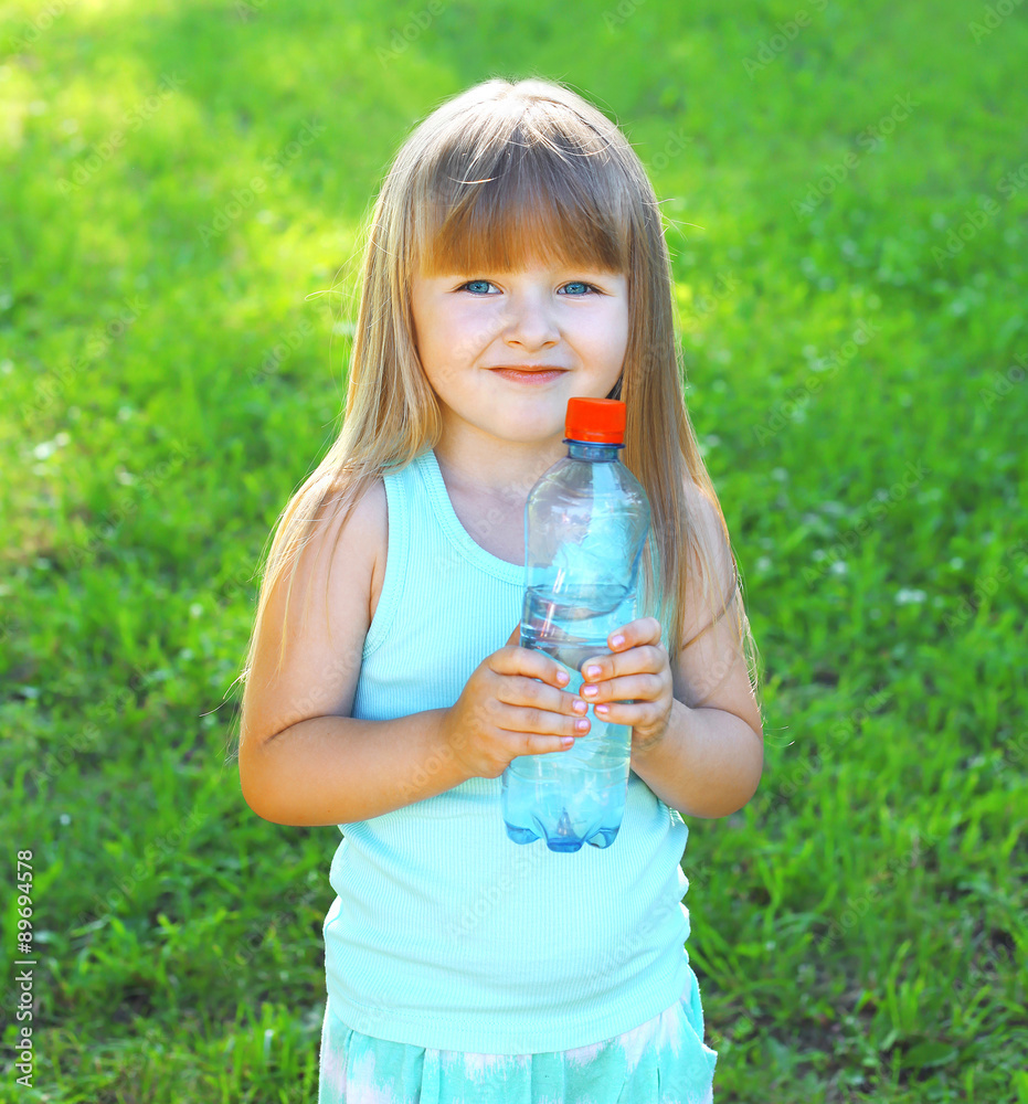 Happpy smiling child and plastic bottle with water on the grass Happpy smiling child and plastic bottle with water on the grass