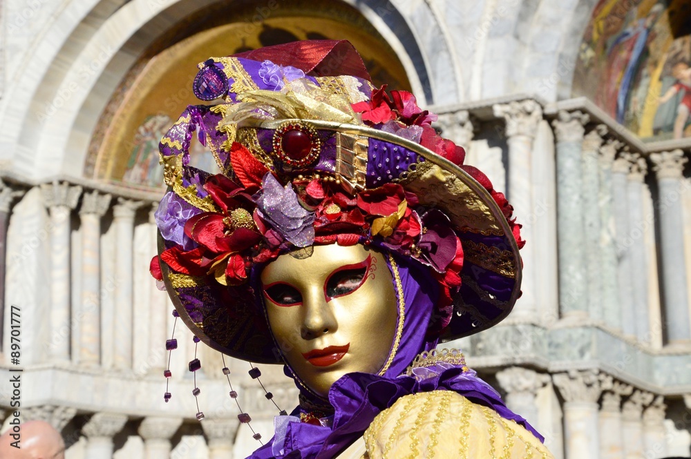 Intense look, golden mask with hat of different geometries in orange and violet tones during the Carnival of Venice, Italy