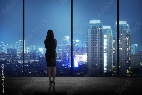 Woman standing in his office looking at the city at night