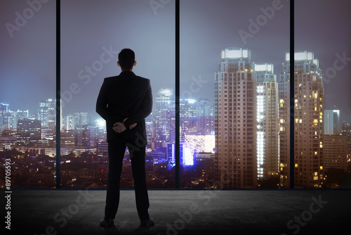 Man standing in his office looking at the city at night