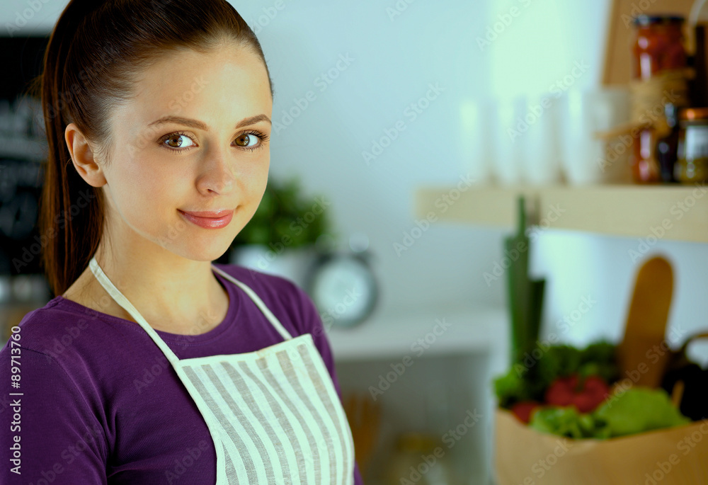 Young woman standing in her kitchen near desk with shopping bags Young woman standing in her kitchen near desk with shopping bags